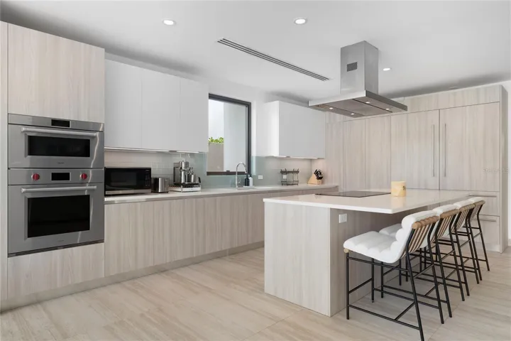 The open kitchen connects seamlessly to the living and formal dining areas, opening to a covered terrace, pool, and outdoor kitchen for effortless indoor-to-outdoor living with beautiful views of the golf driving range