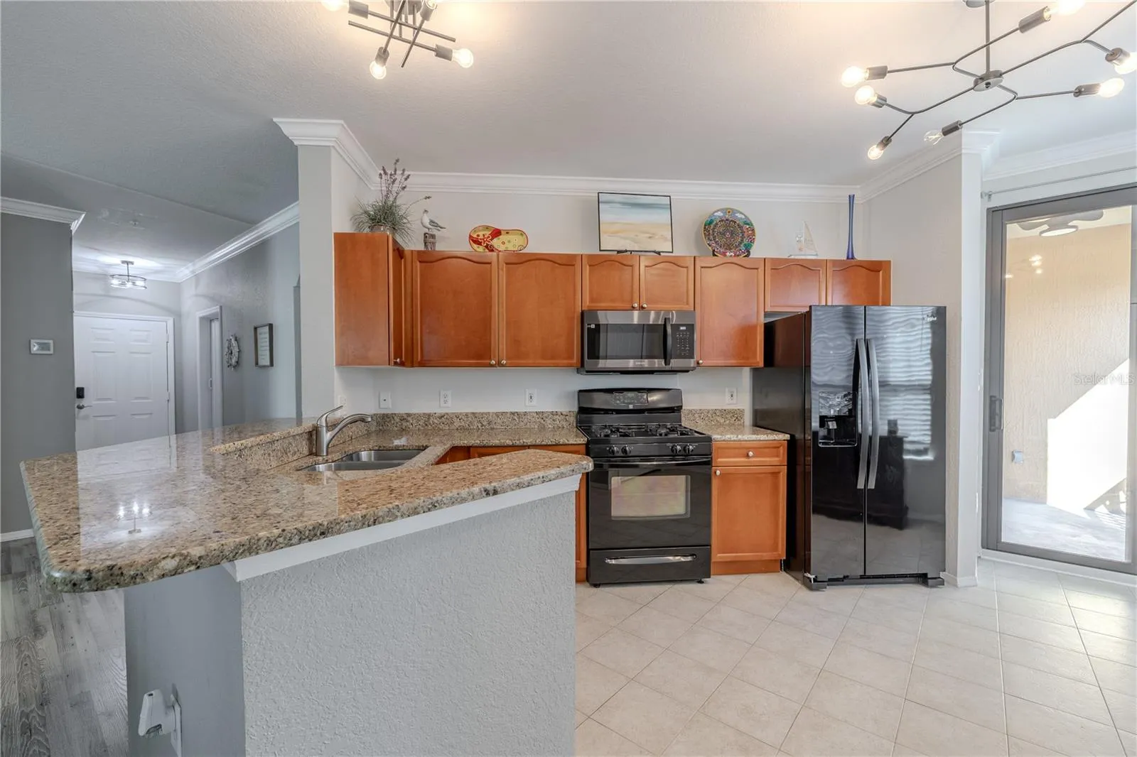 This kitchen view highlights the spacious walk-in pantry with built-in shelving, along with granite countertops, stainless appliances, warm wood cabinetry, and an open sightline to the living area for easy everyday living and entertaining.