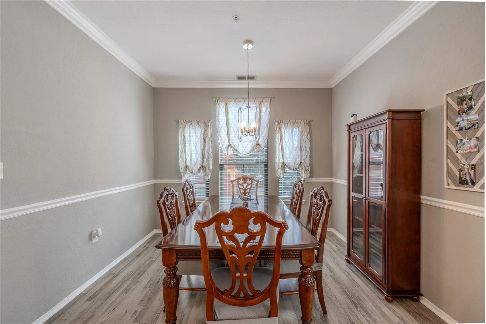An elegant dining room features crown molding, chair rail detailing, wide-plank laminate flooring, and a modern pendant light, creating a refined space perfect for hosting gatherings and formal meals.
