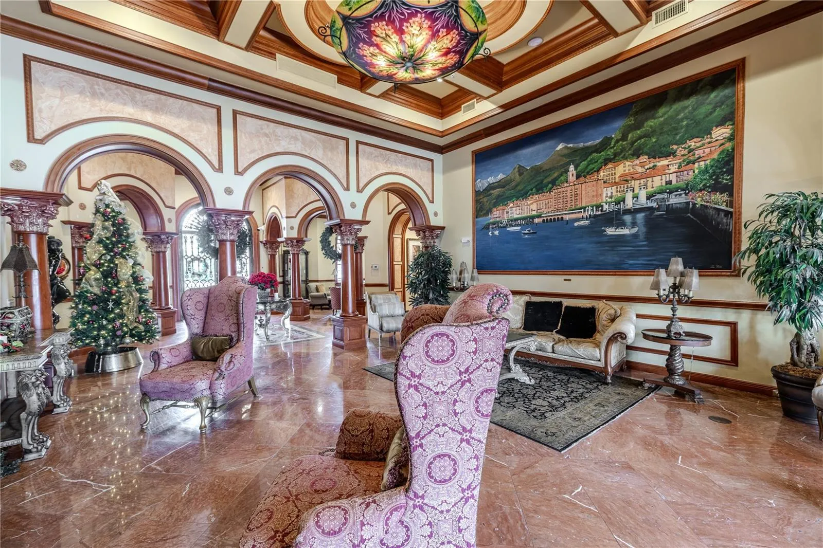 Another view of the grand clubhouse lounge with soaring coffered ceilings, dramatic murals and arched columns, gleaming marble floors, and an elegant fireplace seating area that creates a truly resort-style welcome.