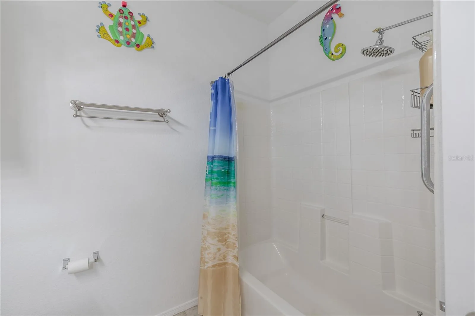 This clean and well-appointed tub/shower combination features crisp white tile surround, built-in shelving, updated fixtures, and a bright, beach-inspired aesthetic that complements the home’s coastal feel.