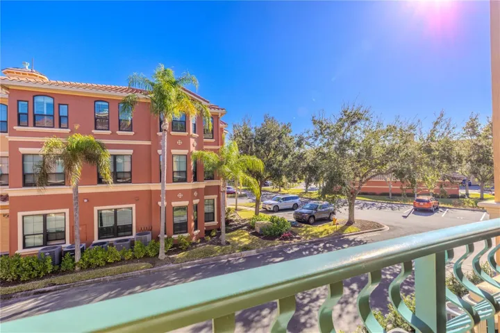 Sunny balcony view overlooking the beautifully maintained, palm-lined community with nearby parking and charming Mediterranean-style architecture.