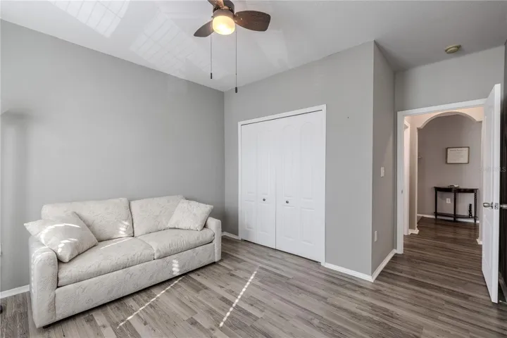 This view of the bright second bedroom features multiple windows for natural light, neutral finishes, wood-look laminate flooring, built in closet, and ample space to function comfortably as a guest room, home office, or flex space.