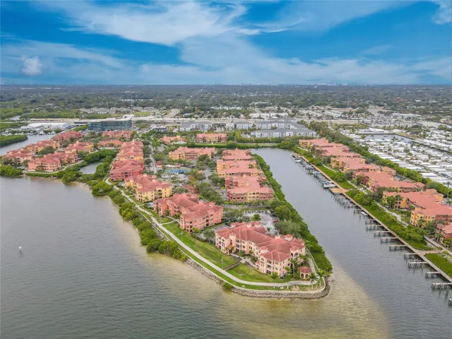 Another elevated aerial waterside view highlights the Mediterranean-style architecture of the Grand Bellagio community, showcasing tile-roofed buildings, palm-lined grounds.
