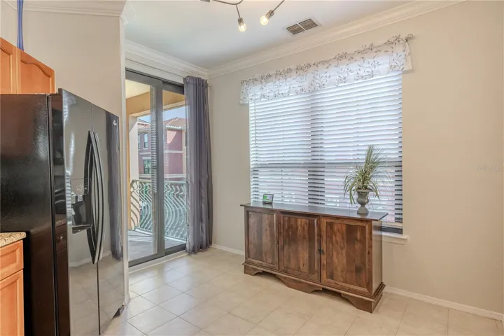 Natural light fills this eat-in kitchen area, featuring a large window, tile flooring, modern lighting, and sliding glass doors that open to the private balcony for easy indoor–outdoor living.