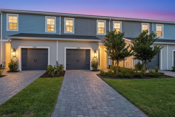 Attractive two-story townhome exterior with coastal-inspired finishes, paver driveway, and warm architectural lighting.