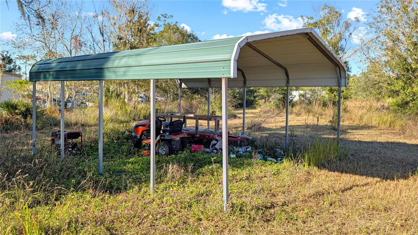 Covered Carport on the very Left, or West, Side of the land that your driveway will go past. Existing on-Site Shipping Container for extra Storage is visible in the distance in the right-center of picture.