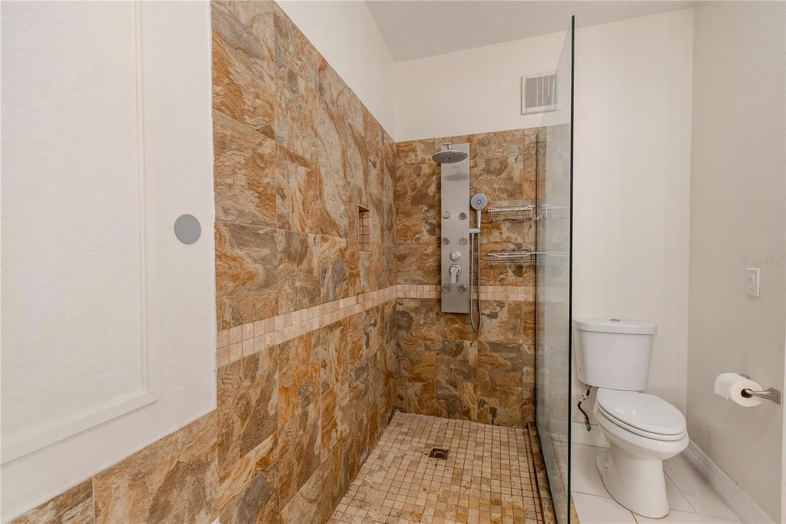 The primary en-suite bathroom walk-in glass-enclosed shower features natural stone tile, a built-in niche, and a multi-function shower system for a true retreat experience.