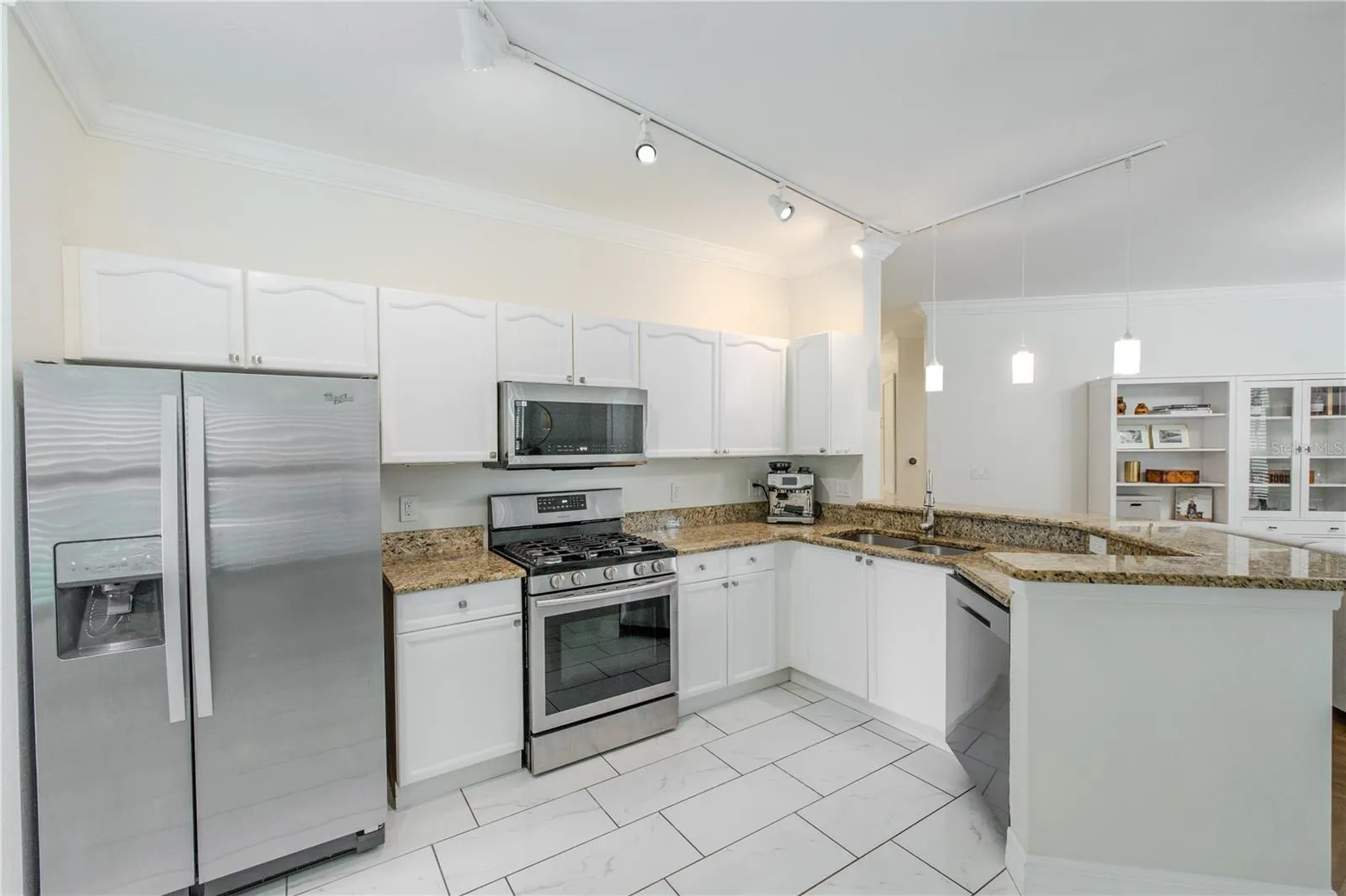 Stainless steel appliances—including a gas range, built-in microwave, refrigerator, and dishwasher—are thoughtfully arranged for efficiency. A double-basin sink with a gooseneck faucet overlooks the living area, reinforcing the kitchen’s open connection to the rest of the home.