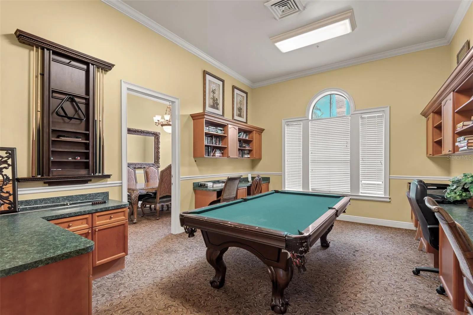 The clubhouse game and lounge room includes a billiards table, built-in counters and cabinetry, and a sunlit arched window—ideal for gathering with neighbors, playing a round of pool, or simply unwinding.