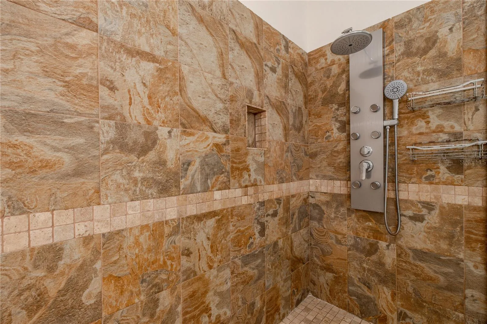 Another view of the primary en-suite bathroom walk-in glass-enclosed shower features natural stone tile, a built-in niche, and a multi-function shower system for a true retreat experience.