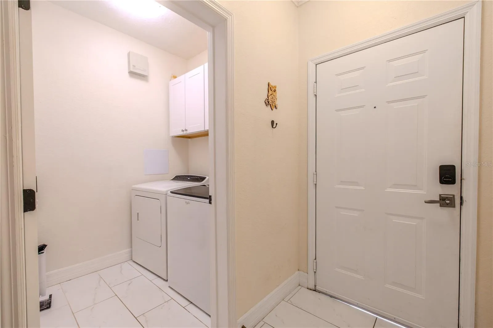The laundry room is neatly tucked away and thoughtfully designed, featuring a full-size washer and dryer with upper cabinetry for convenient storage. Neutral finishes keep the space bright and functional, while the efficient layout makes everyday laundry tasks easy and organized without taking up valuable living space.