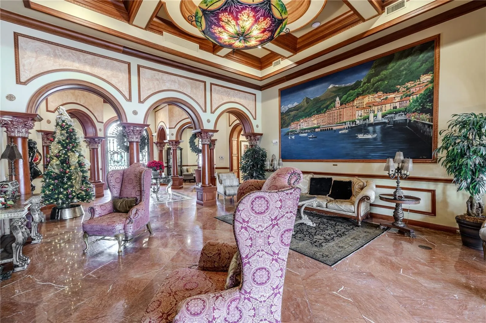 Another view of the grand clubhouse lounge features soaring coffered ceilings, dramatic murals and arched columns, gleaming marble floors, and an elegant fireplace seating area—offering a warm, truly resort-style welcome.