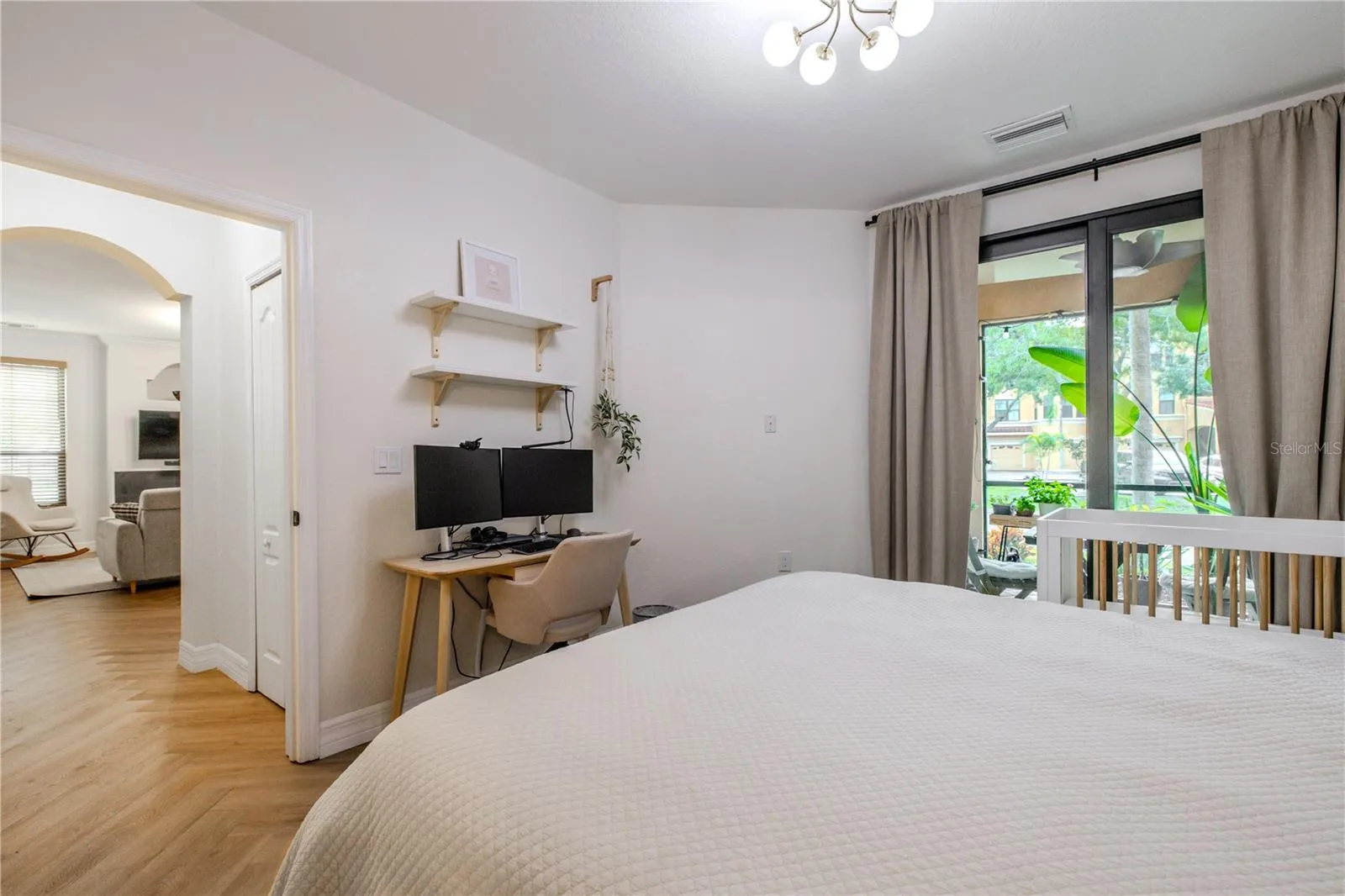 The primary bedroom features soft natural light, a modern statement light fixture, &amp; sliding glass doors opening to the covered patio
