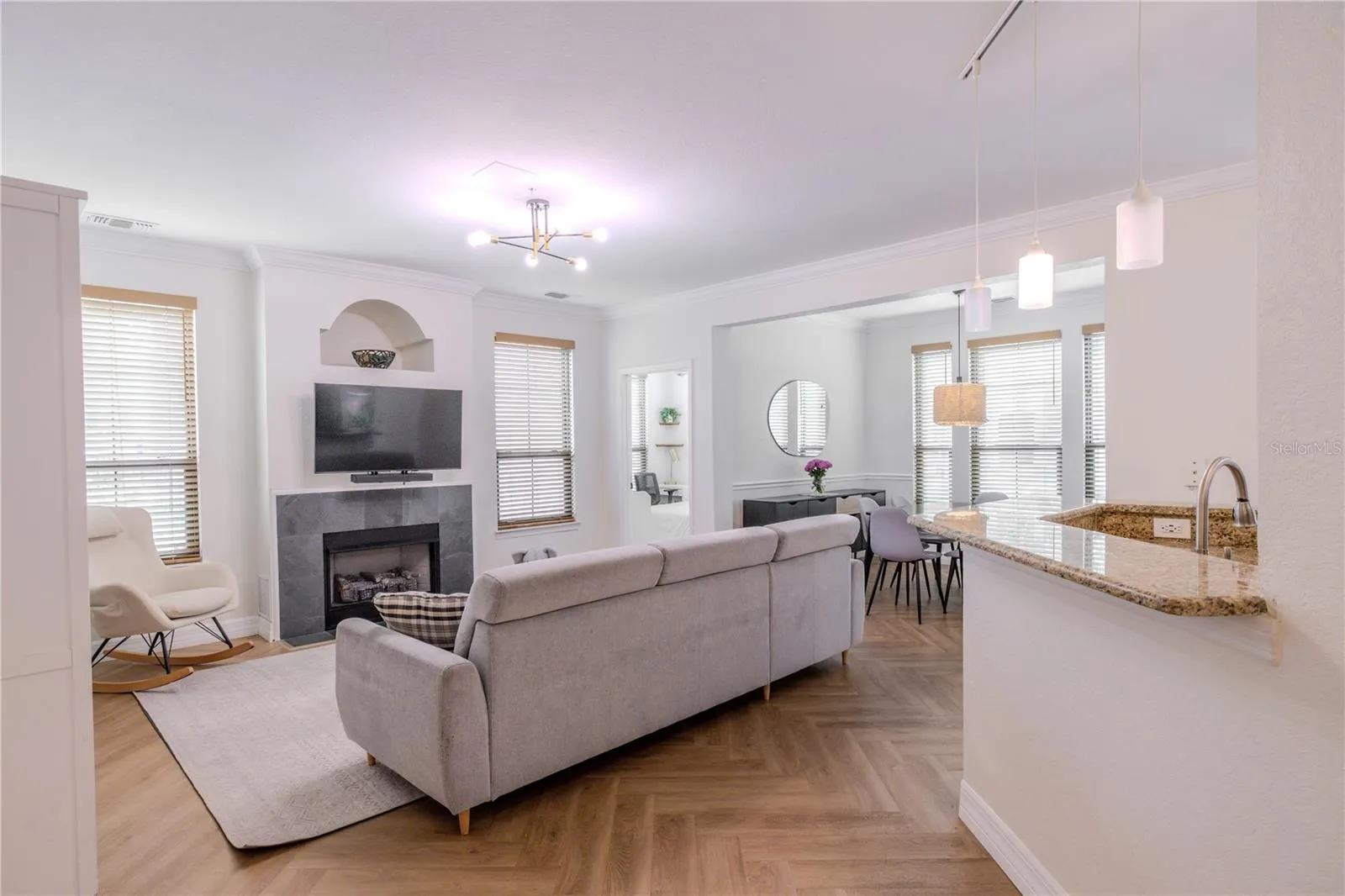 Spacious open-concept living area with chevron luxury vinyl plank flooring, a modern fireplace, and seamless flow into the dining space beyond.