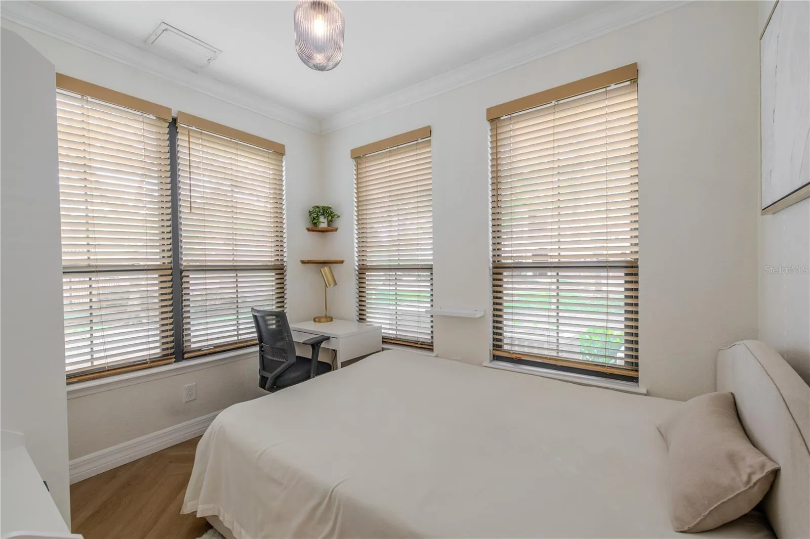 A sunlit den with crown molding and multiple windows creates a flexible, inviting space perfect for a home office, guest accommodations, or a cozy sitting room