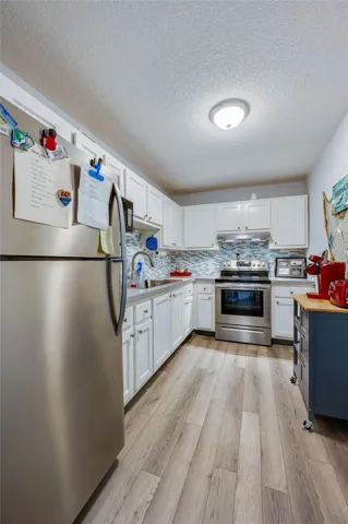 Crisp and functional galley-style kitchen with stainless steel appliances, shaker-style cabinetry, and a mosaic tile backsplash that adds a pop of color and coastal flair.