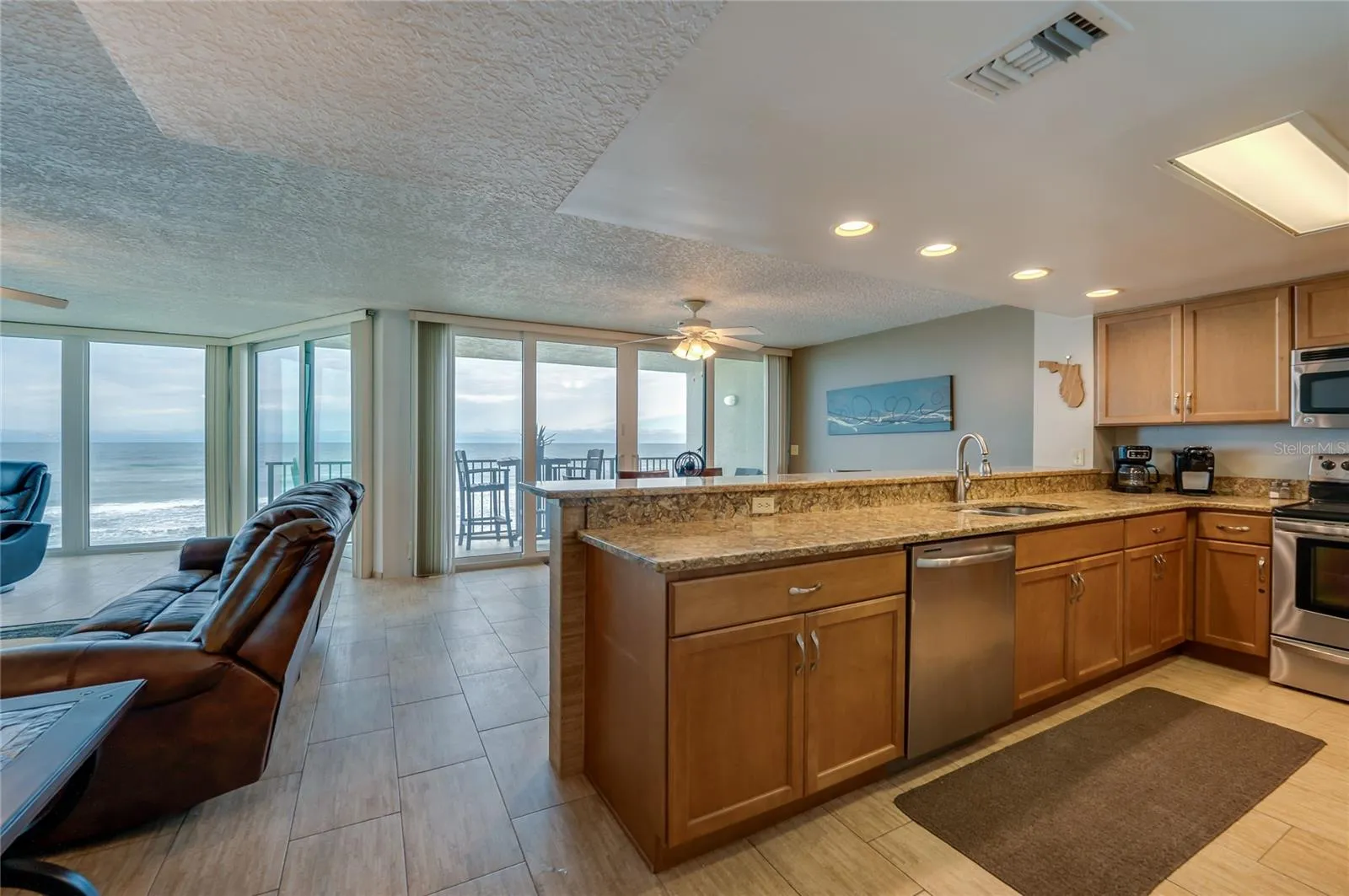 This open kitchen boasts granite countertops, stainless steel appliances, and a breakfast bar overlooking the ocean-facing dining space—perfect for entertaining or everyday living.