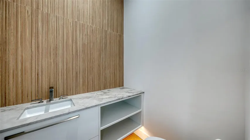 Powder room upon second floor entry features custom suspended cabinetry and large format "wood" tile