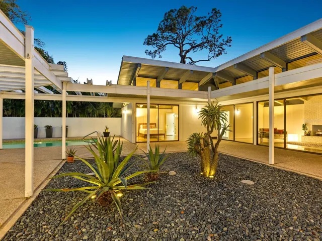 View from kitchen through courtyard at dusk garden to pool on left and rooms center and right