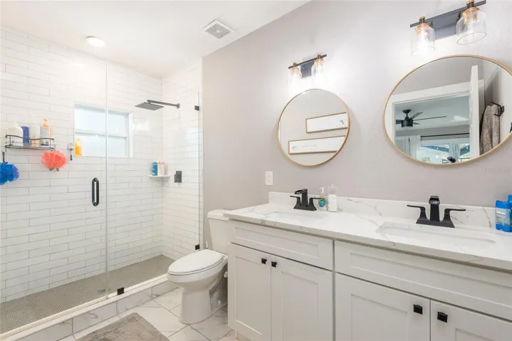 Primary's large ensuite bathroom has dual sinks, stone counters, and walk-in shower with rain shower head