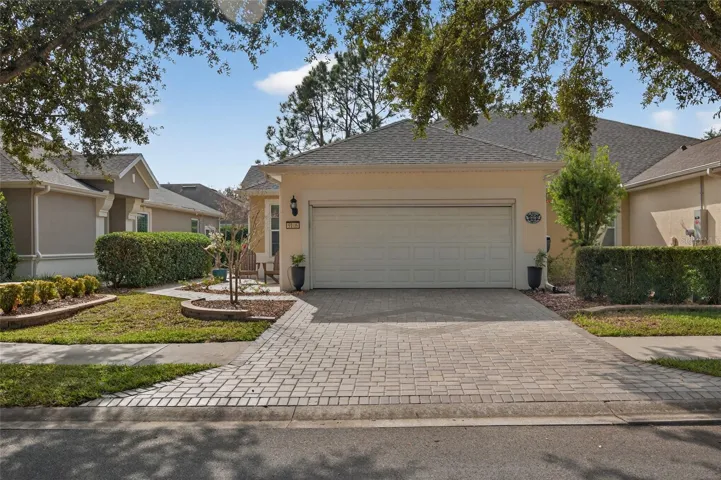 Villa front with 2 car garage, pavers and shade trees.
