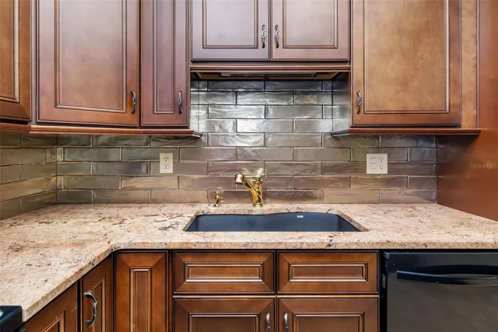 Upgraded kitchen with granite countertops, tile backsplash, and custom cabinetry in this Bradenton 55+ condo