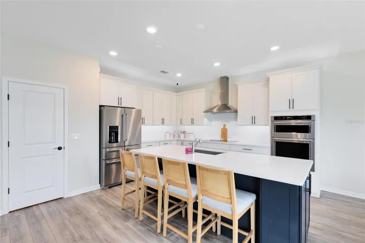 Chef’s kitchen with crisp white quartz countertops, KitchenAid gourmet stainless appliances, 42” soft-close cabinets and drawers, a large granite island with a large granite sink, and an oversized walk-in pantry.
