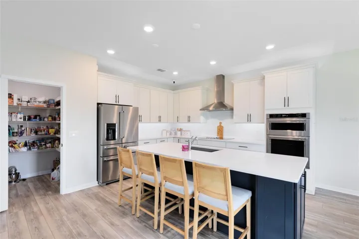 Chef’s kitchen with crisp white quartz countertops, KitchenAid gourmet stainless appliances, 42” soft-close cabinets and drawers, a large granite island with a large granite sink, and an oversized walk-in pantry.