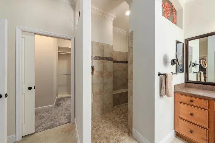 PRIMARY ENSUITE BATHROOM - Walk-in CLOSET #1 (L) with POCKET DOOR ACCESS, entrance to ROMAN SHOWER (center) and L shaped vanity w/ framed mirrors & dual sinks (R).