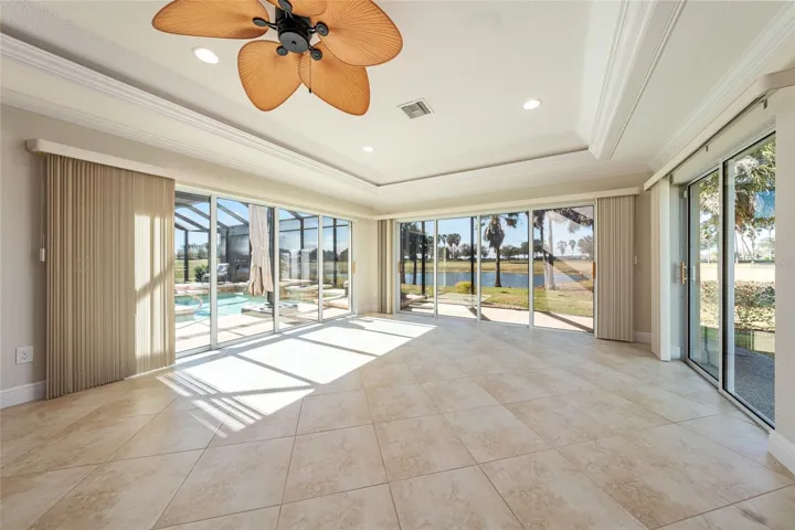 View of the back half of the MULTIPURPOSE ROOM that flaunts CROWN MOLDING, lighted TRAY CEILING with accent molding, recessed lighting, ceiling fan, 20" x 20" diagonal set, TILE FLOORING, and 3 sets of SLIDING GLASS DOORS that frame that gorgeous Evans Prairie Championship GOLF COURSE FRONTAGE/WATER VIEW! Note that golf cart path runs behind the pond.