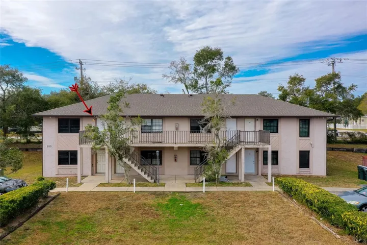 Upstairs unit highlighted in this well-maintained two-story complex with mature trees, exterior stair access, and a neatly landscaped front lawn.