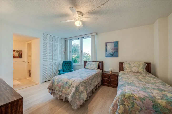Bright secondary bedroom with large closet storage and tropical views through oversized windows.