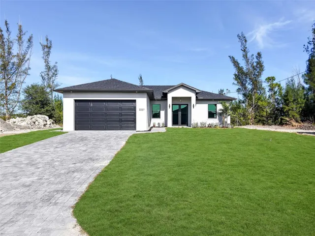 View of front facade featuring a front yard,decorative driveway, stucco siding, an attachedgarage, and roof with shingles