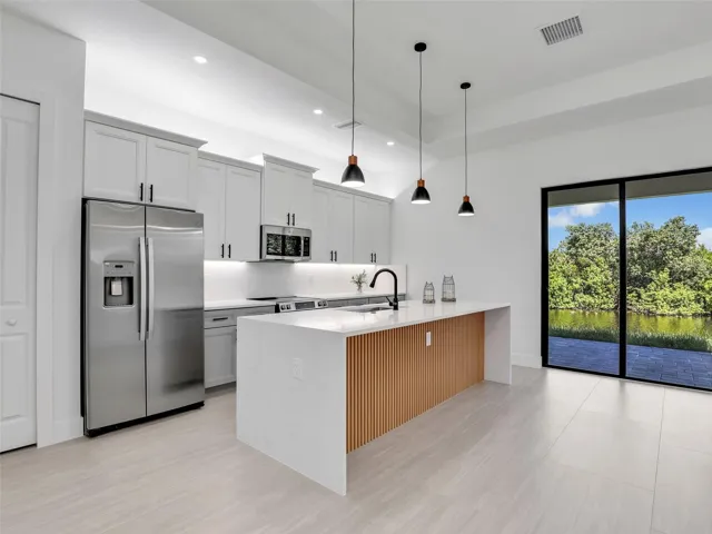 Kitchen featuring stainless steel appliances,hanging light fixtures, light stone counters,recessed lighting, and white cabinetry