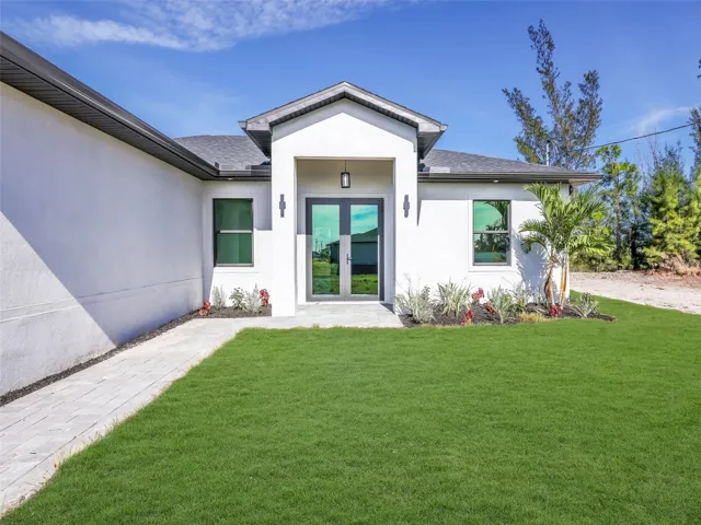 Doorway to property with french doors, stuccosiding, and a lawn