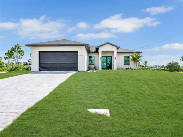 Prairie-style house featuring stucco siding,decorative driveway, a front yard, and anattached garage