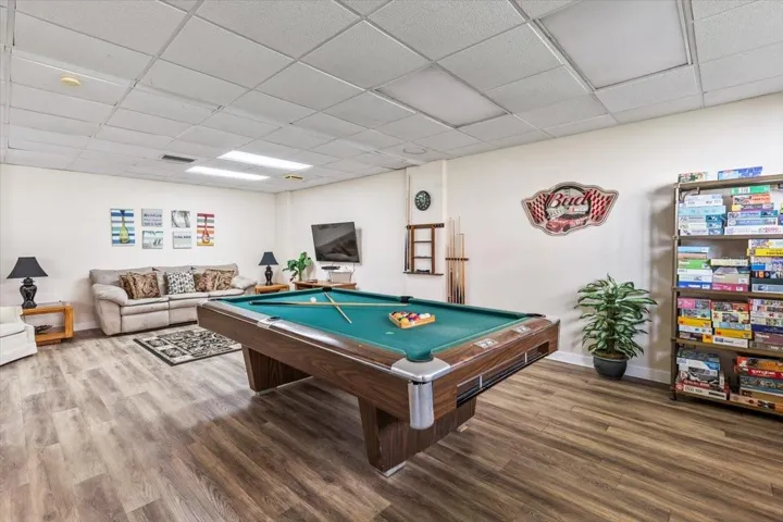 Spacious community game room featuring a full-size billiards table, cozy lounge seating, wall-mounted TV, and a library of board games—perfect for relaxing or entertaining guests.