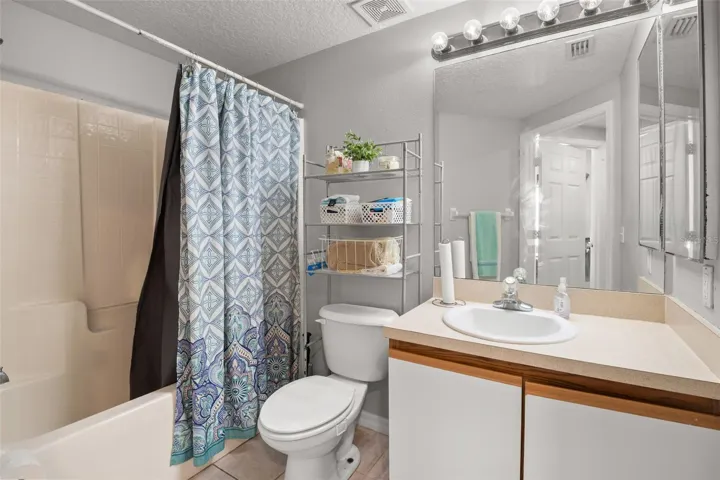 Secondary full bathroom featuring a single-sink vanity with ample counter space and storage below, a large wall mirror with overhead lighting, and a tub/shower combination. The neutral finishes create a bright, functional space ideal for guests or everyday use within the split-bedroom layout.