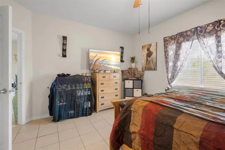 Light-filled primary bedroom featuring ceramic tile flooring and a generous layout that accommodates full-size furnishings with ease. A large window provides natural light, while the neutral color palette offers flexibility for any décor style. The suite includes direct access to the en suite bath and walk-in closet, enhancing privacy and everyday convenience within the split-bedroom floor plan.