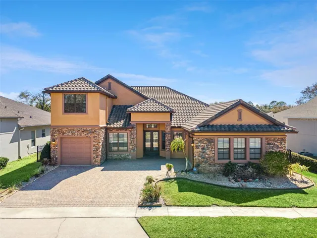 Elegant Sanford, FL home with striking stone façade, barrel tile roof, and an expansive paver driveway that enhances its upscale curb appeal.