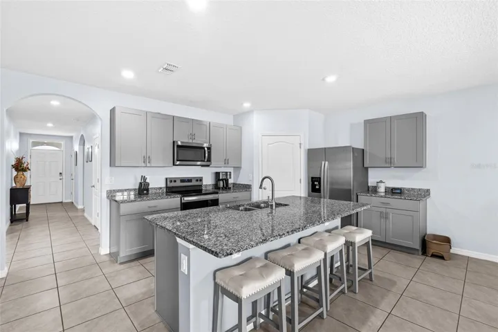 The heart of the home is the modern kitchen, featuring a fresh color palette with gray cabinetry, complementary granite countertops, STAINLESS STEEL APPLIANCES, pantry storage, and a large ISLAND with bar seating, all open to the living and dining areas – ideal for everyday living or for those who love to entertain!