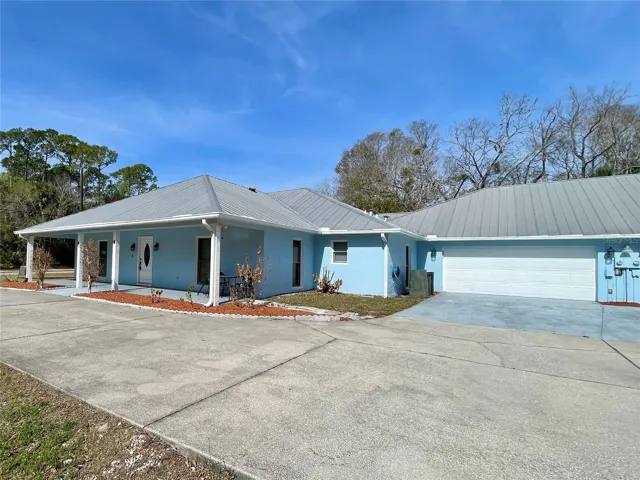 This charming home features a light blue exterior with crisp white trim and a durable metal roof. The extended driveway and attached two-car garage provide ample parking and everyday convenience.