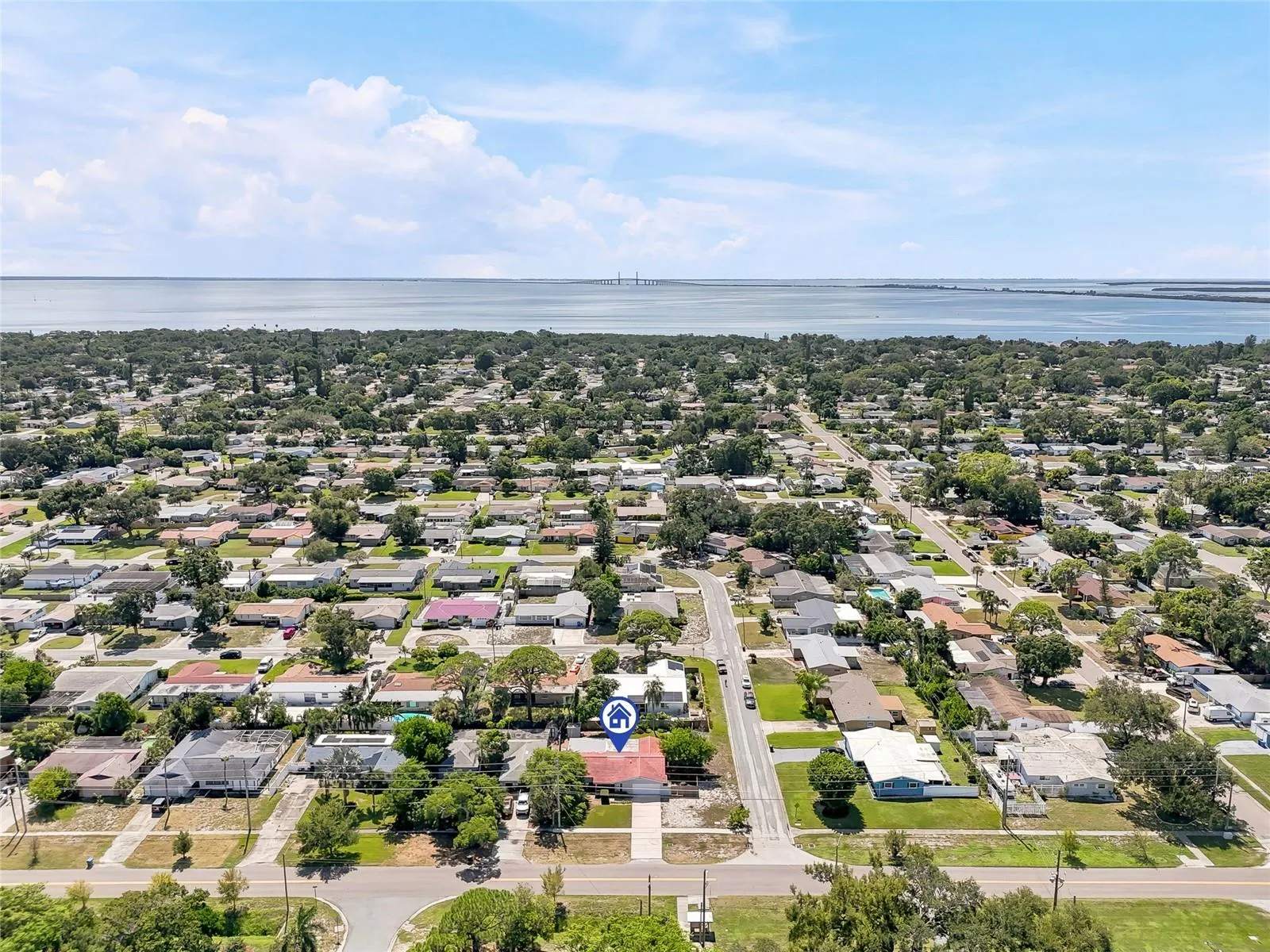 A wider aerial perspective places the home within its leafy St. Petersburg neighborhood, with the bay and Sunshine Skyway Bridge on the horizon.