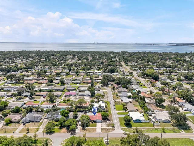 A wider aerial perspective places the home within its leafy St. Petersburg neighborhood, with the bay and Sunshine Skyway Bridge on the horizon.