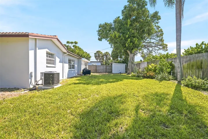 Stretch out in the sunshine or settle beneath the trees, with open lawn, established planting beds, and wood fencing framing the backyard.
