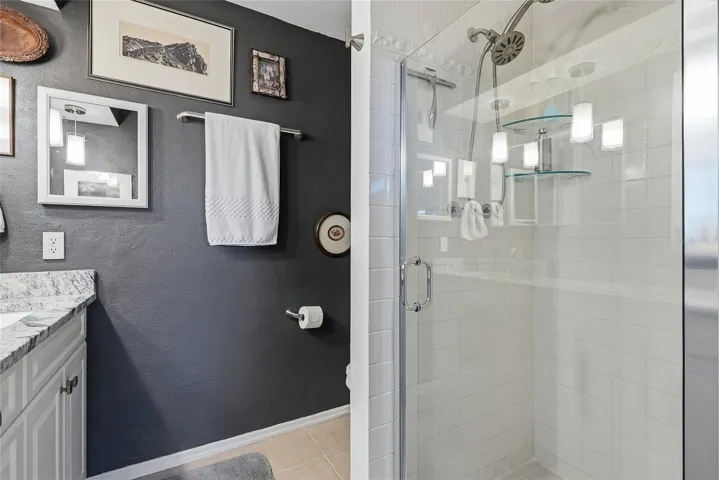 The primary bath features a glass-enclosed shower with classic white tile, glass corner shelves, and a convenient handheld showerhead.