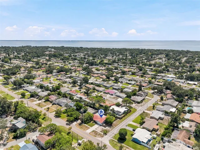 An elevated view highlights the home’s corner lot and tree-filled surroundings, with the bay forming a scenic backdrop beyond the neighborhood.