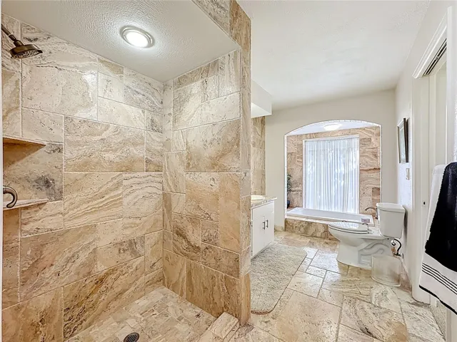 Spacious primary bathroom with a walk in shower with custom travertine tile finishes , large sunkin tub for relaxing after a long day.