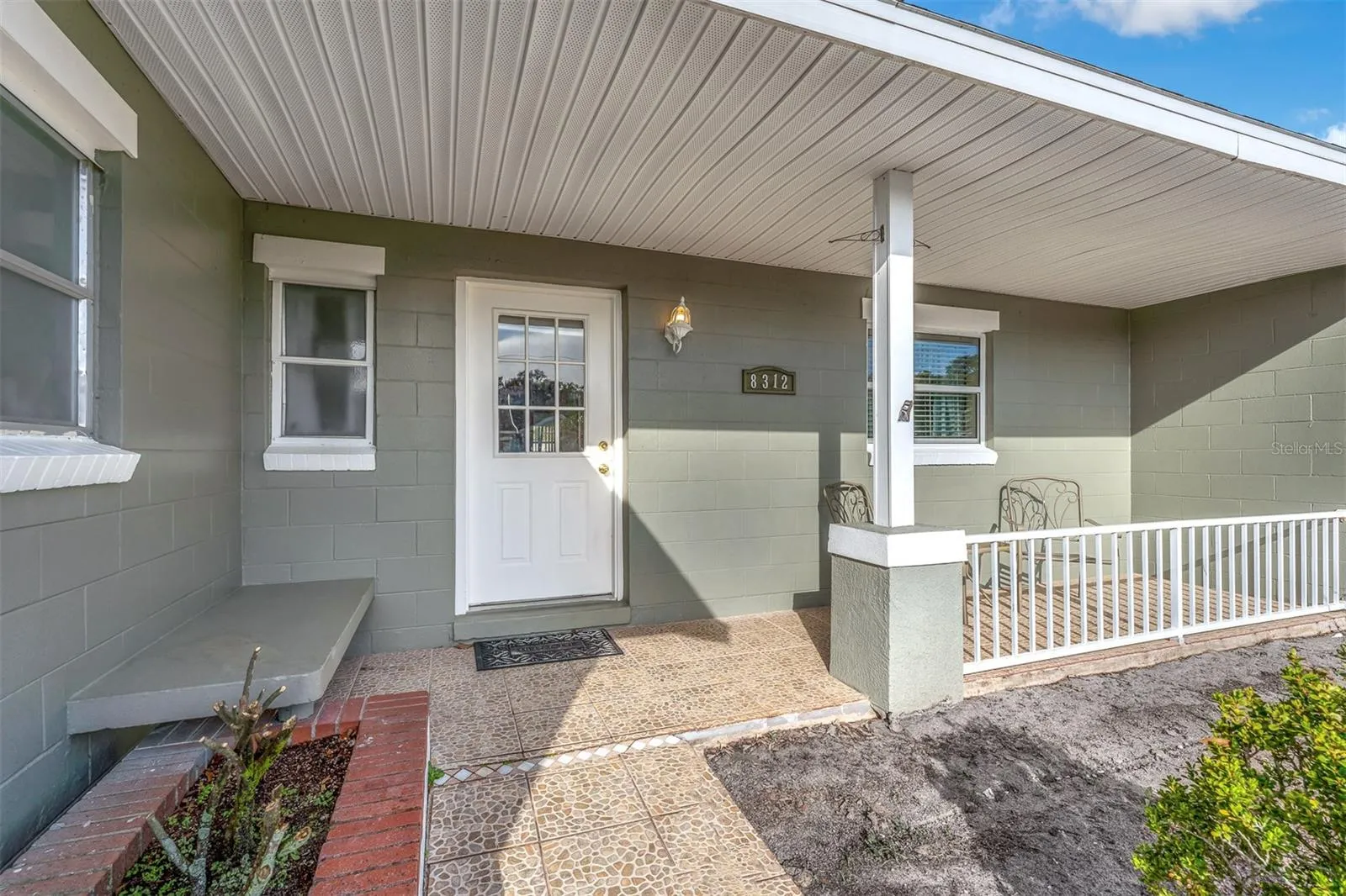 Covered entry with tile flooring, white railing, and space for seating. Features a decorative front door and exterior lighting.